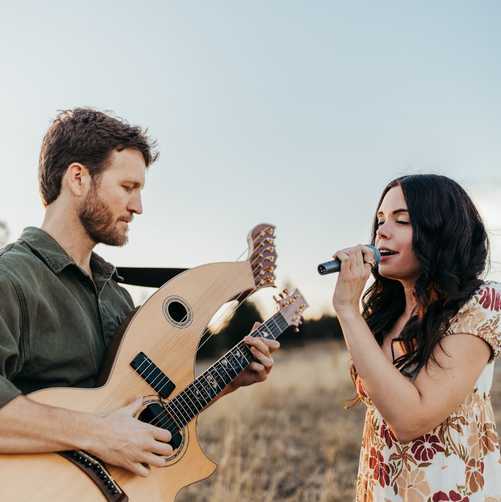 Man playing guitar and woman singing outdoors in a field