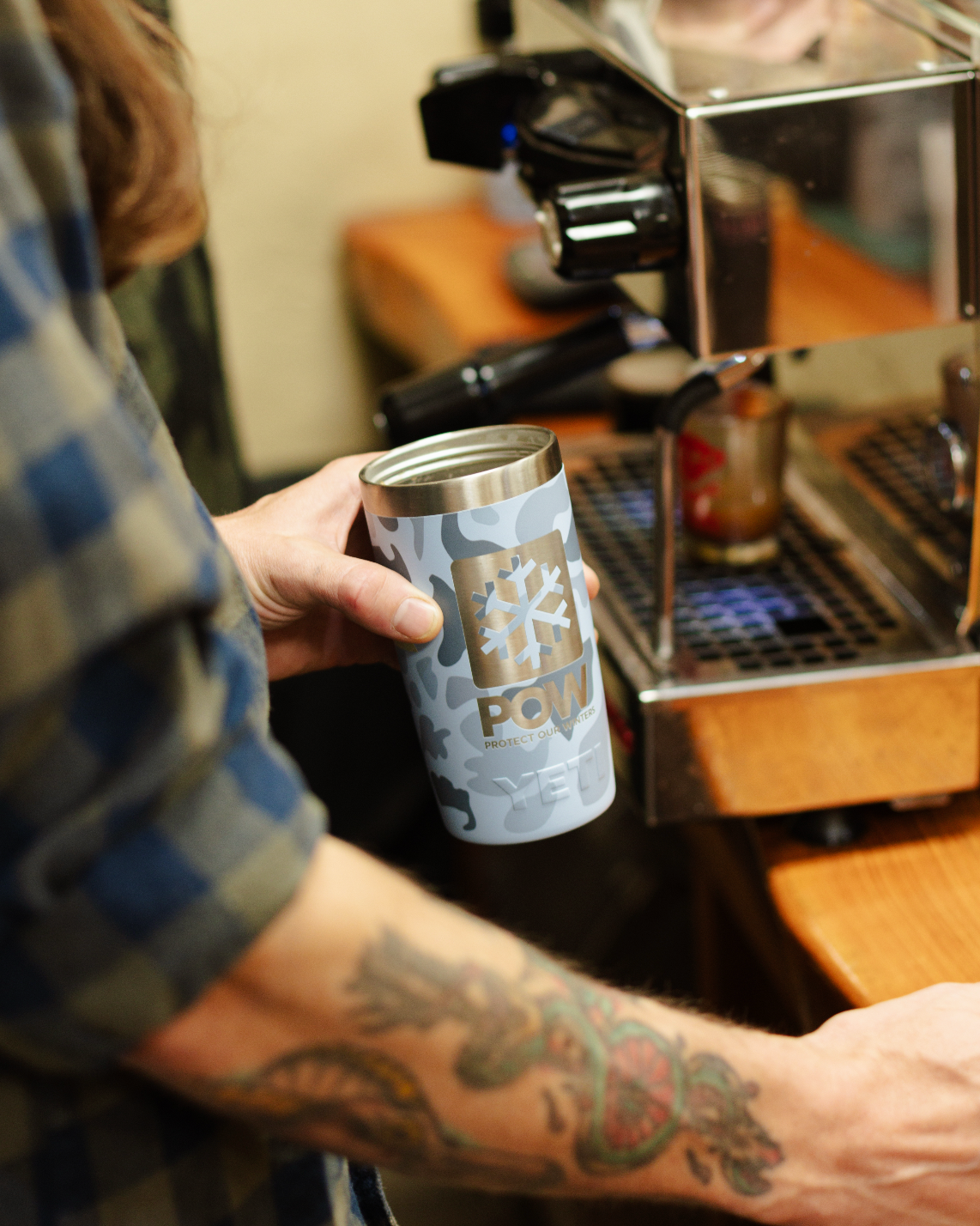 Person holding a coffee cup with the Protect Our Winters logo