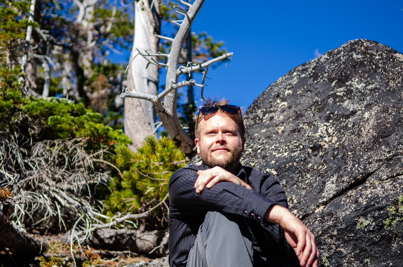 Man sitting on a rock in a forested area with clear blue sky